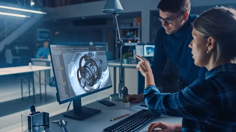 Two engineers reviewing a mechanical assembly model on a desktop monitor.